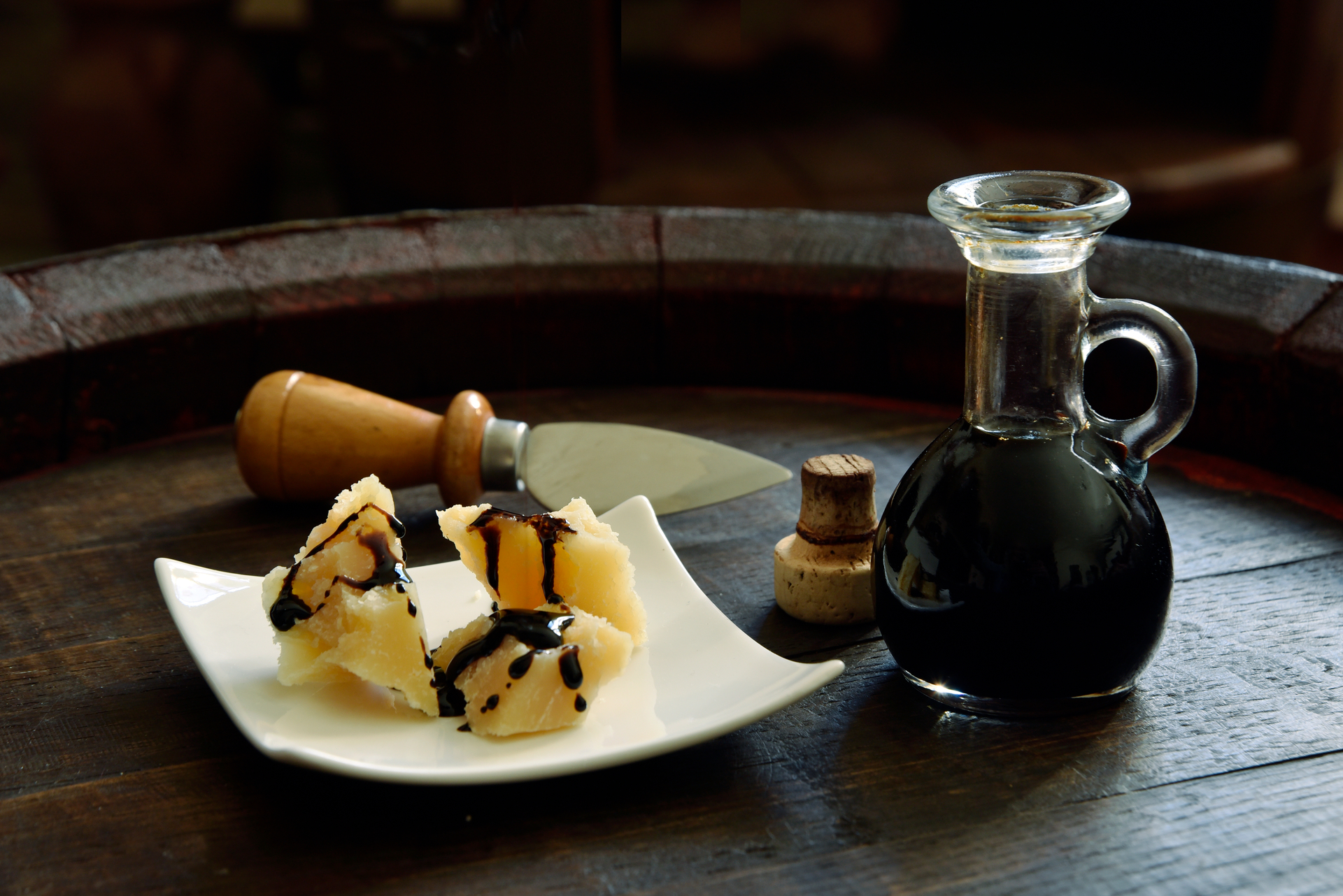Parmigiano and balsamic vinegar served on a plate, accompanied by a traditional Parmesan knife and an open bottle of vinegar